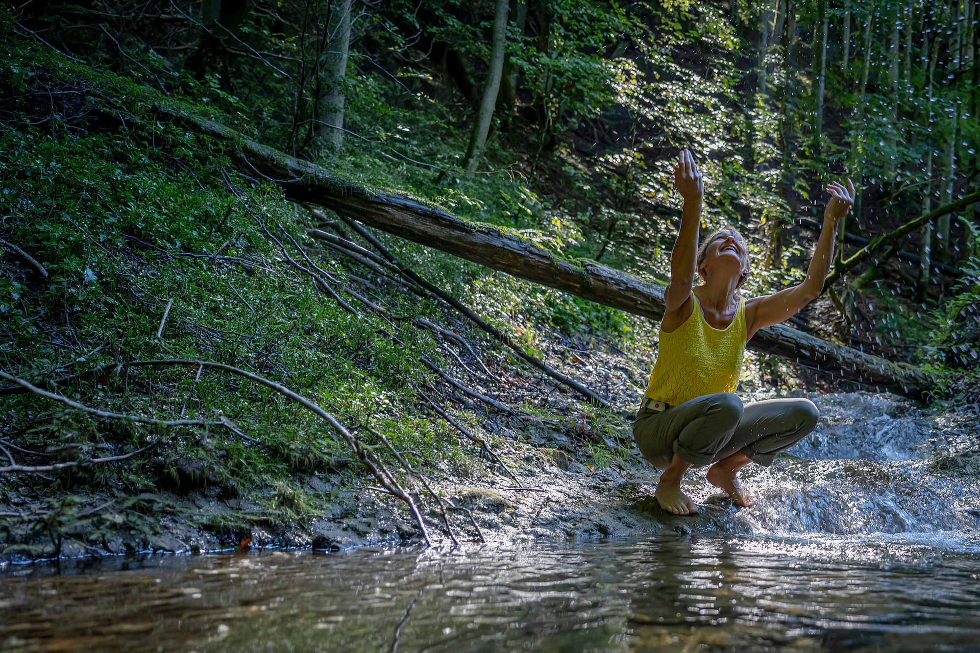 Olga Gaile auf einem Baumstamm über einem Waldbach Olga Gaile in der Natur – Seminare und Workshops